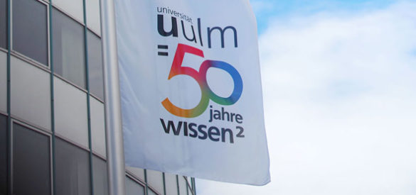 Wehende Fahnen vor der Universität Ulm mit dem Logo der Uni Ulm 50 Jahre Wissen