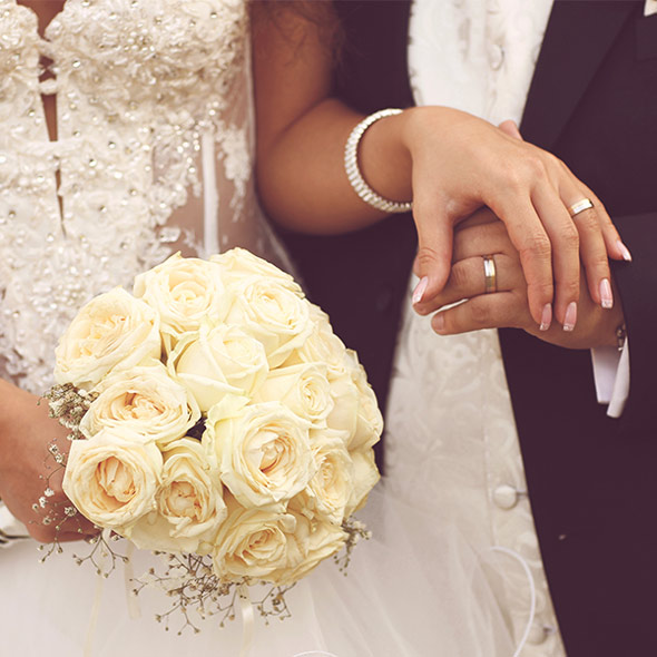 Ein frisch verheiratetes Ehepaar hält sich die Hände, zeigt die RInge und einen Strauß